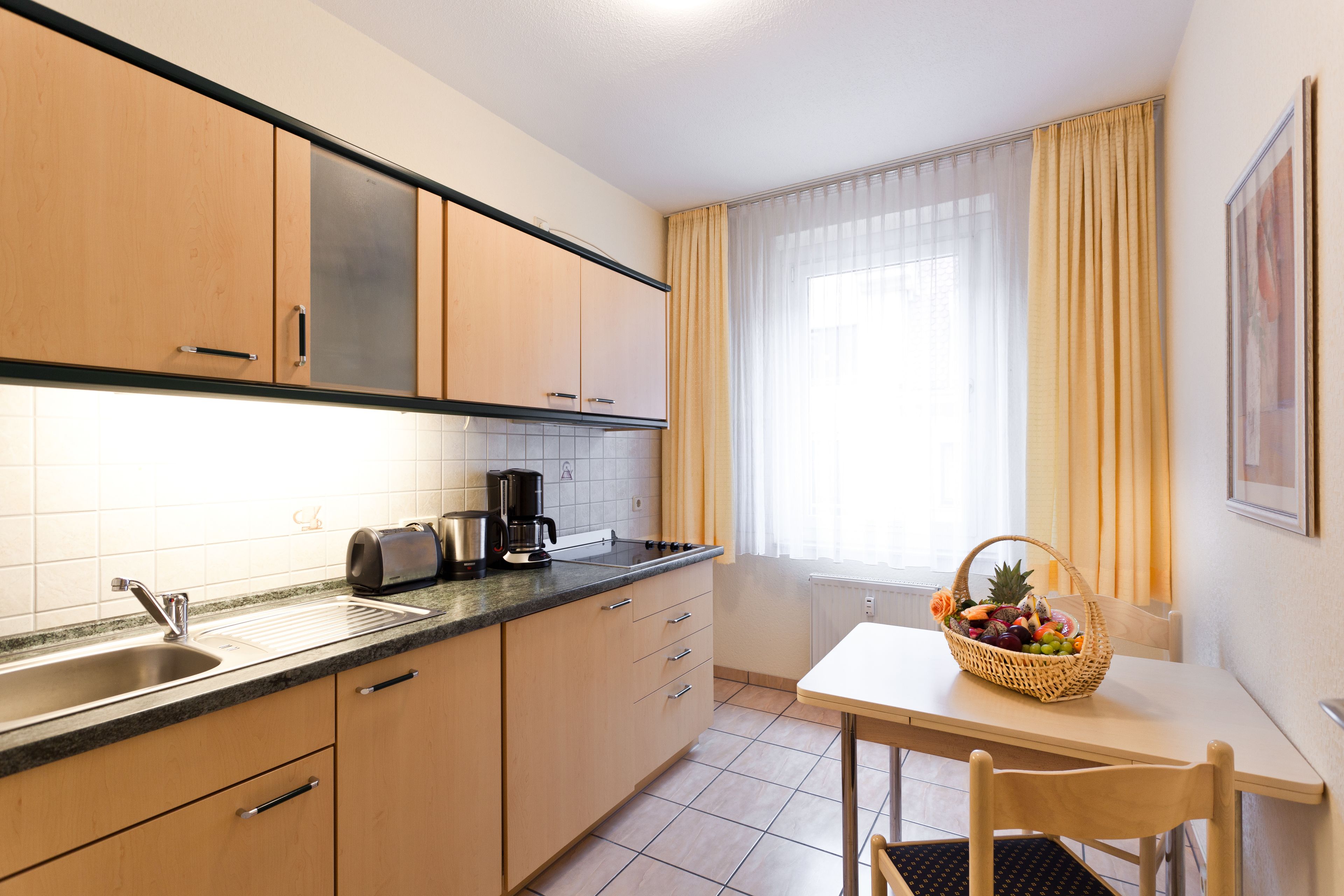 A kitchen with a sink, stove, and a table with a fruit basket.