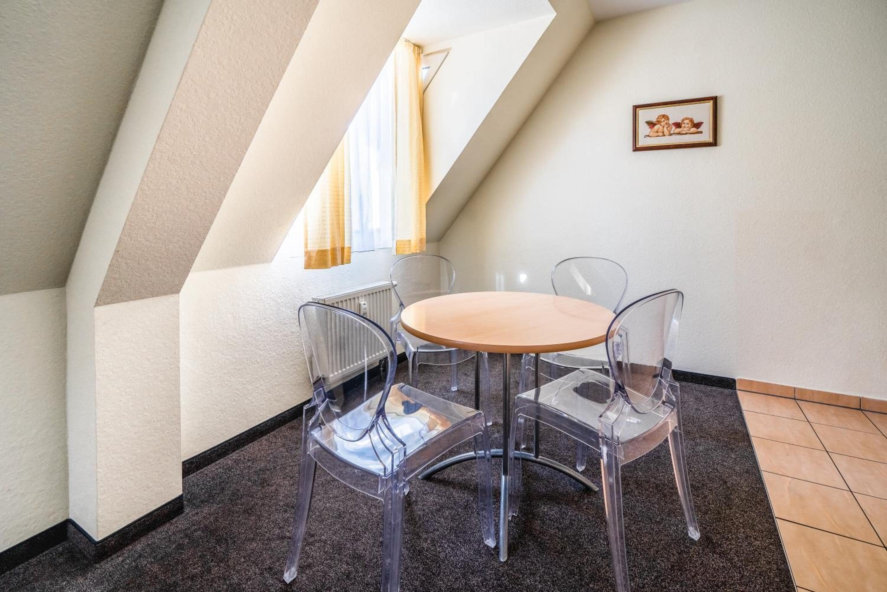 A dining area with a round table and four clear chairs, a radiator, and a picture on the wall.