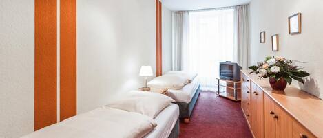 Une chambre d’hôtel avec deux lits, un téléviseur, une commode en bois et une fenêtre avec des rideaux.