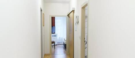 Un pasillo estrecho con suelo de madera y paredes blancas, que conduce a una habitación con cama y ventana.