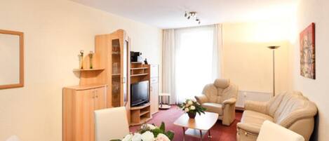 A living room with a TV, sofa, armchair, and a wooden cabinet.