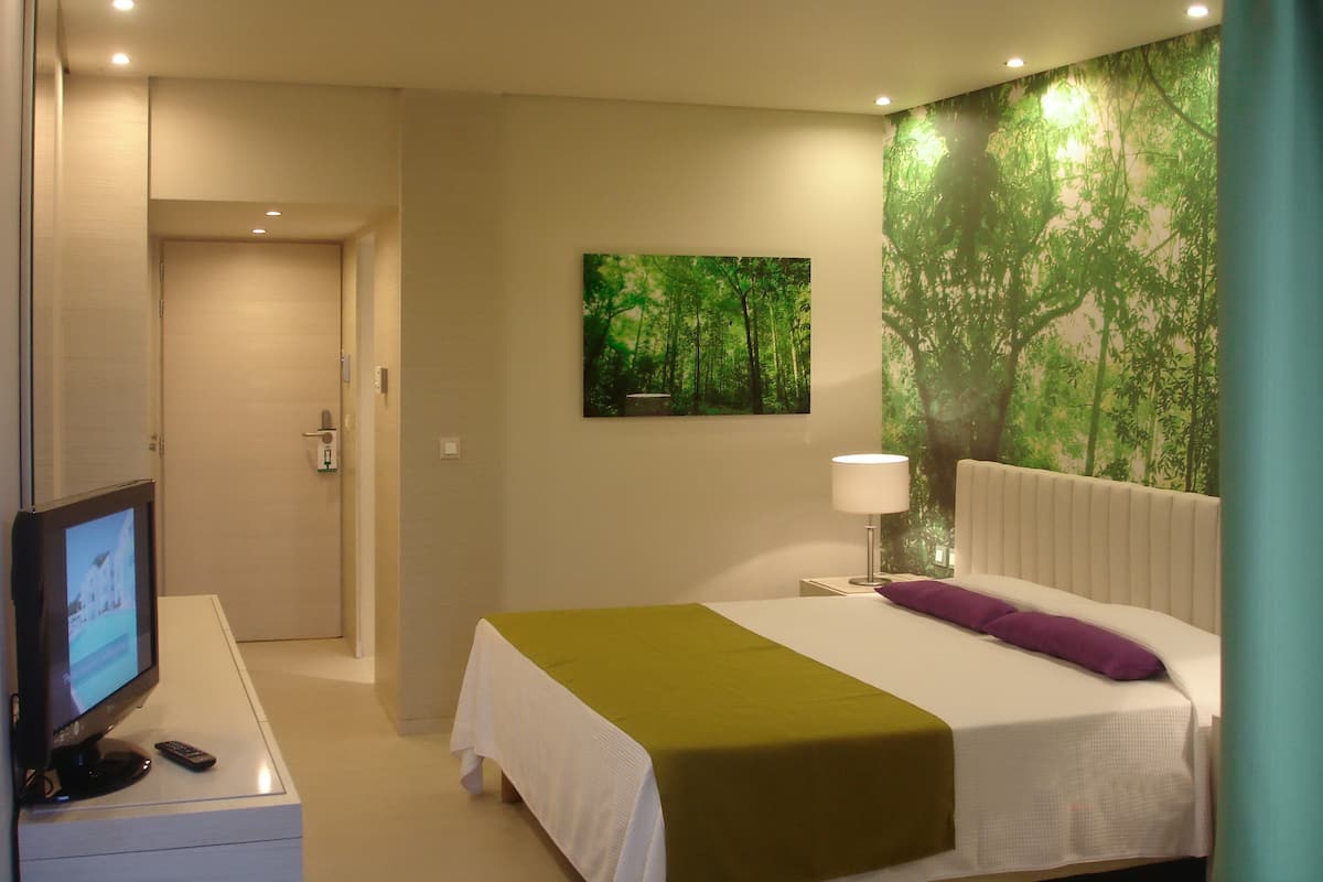 Ein Hotelzimmer mit einem Bett, einem Fernseher, einem Waldbild und einem Nachttisch.