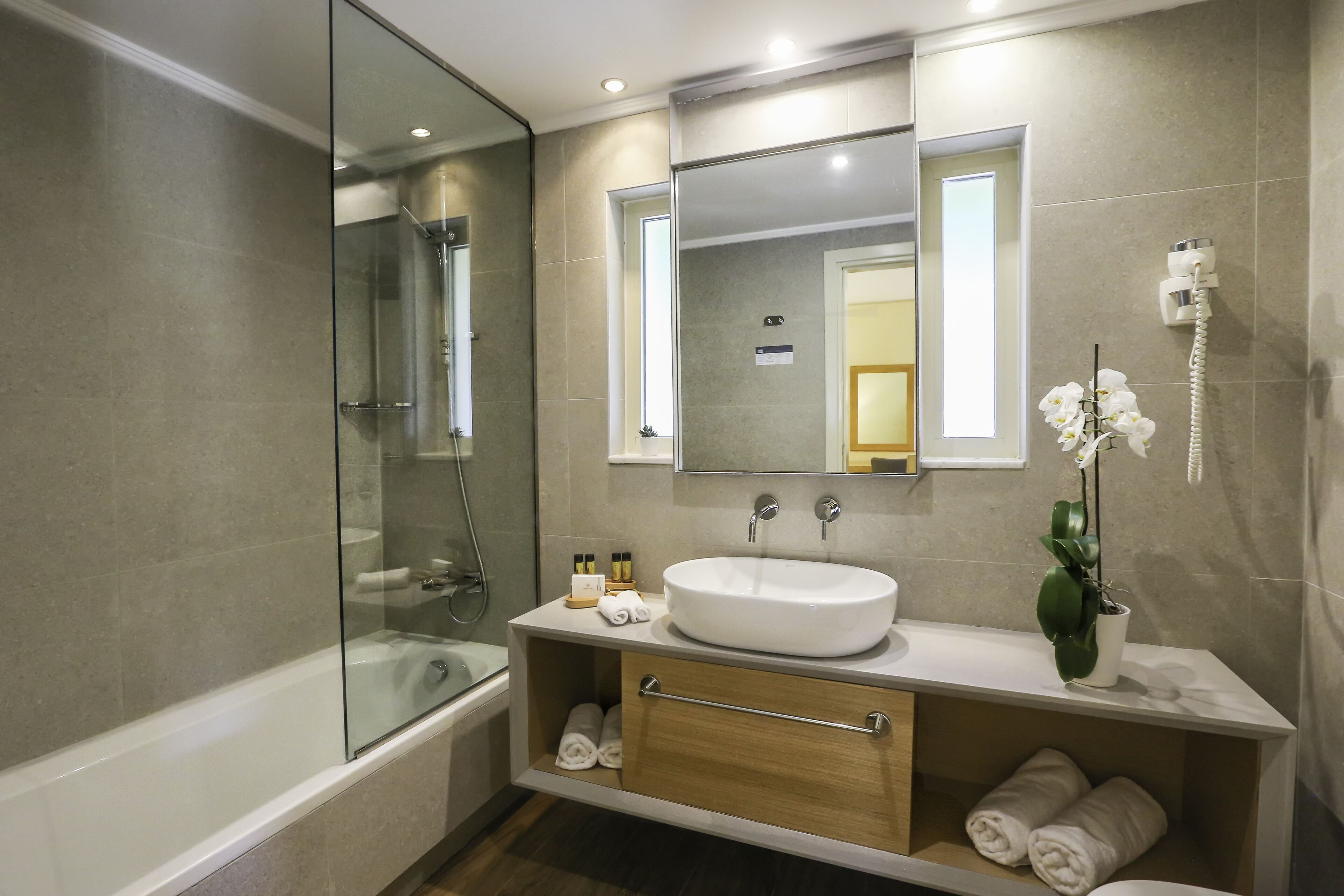 Un baño moderno con ducha de vidrio, un lavamanos blanco y un espejo encima.