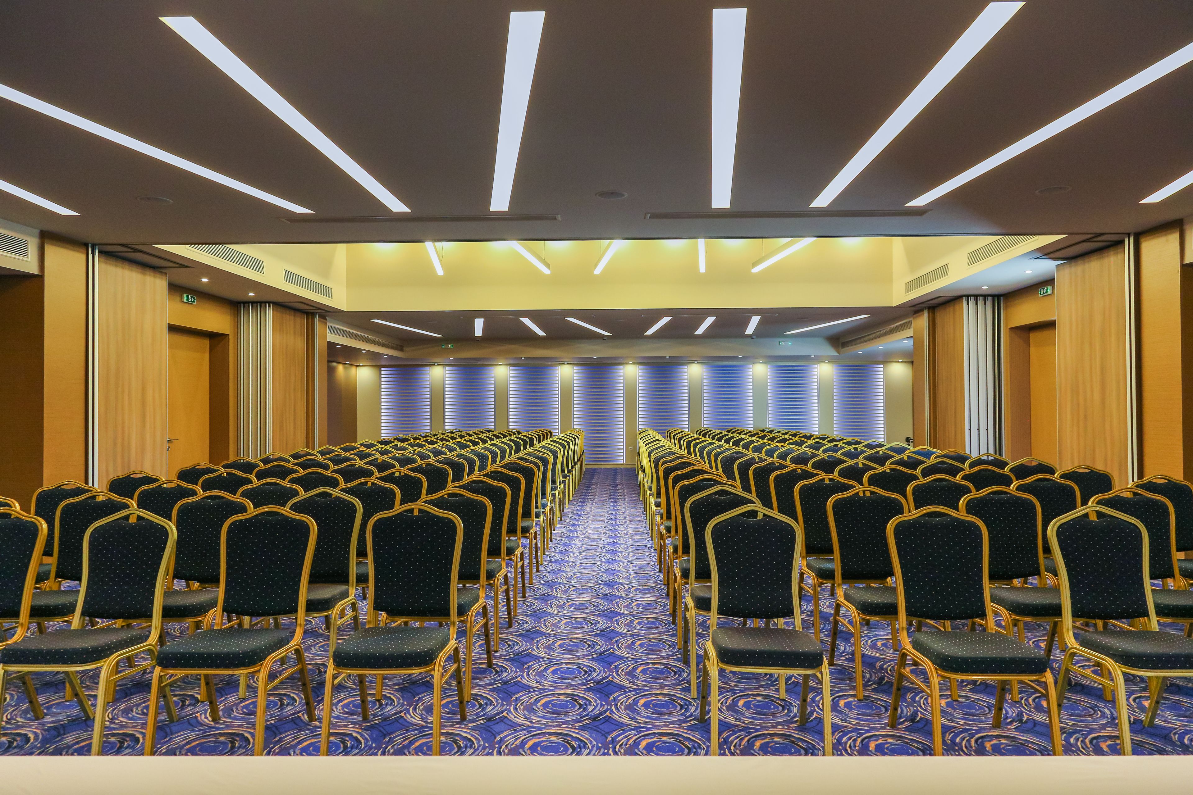 A conference room with rows of chairs, a patterned carpet, and a modern ceiling design.