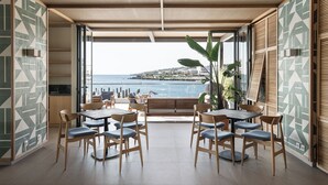 A dining area with a view of the sea, featuring wooden tables and chairs, and a large window.