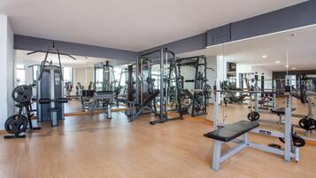 Une salle de sport équipée de divers appareils d’exercice, notamment des machines de musculation et des poids libres, le tout installé sur un plancher en bois.