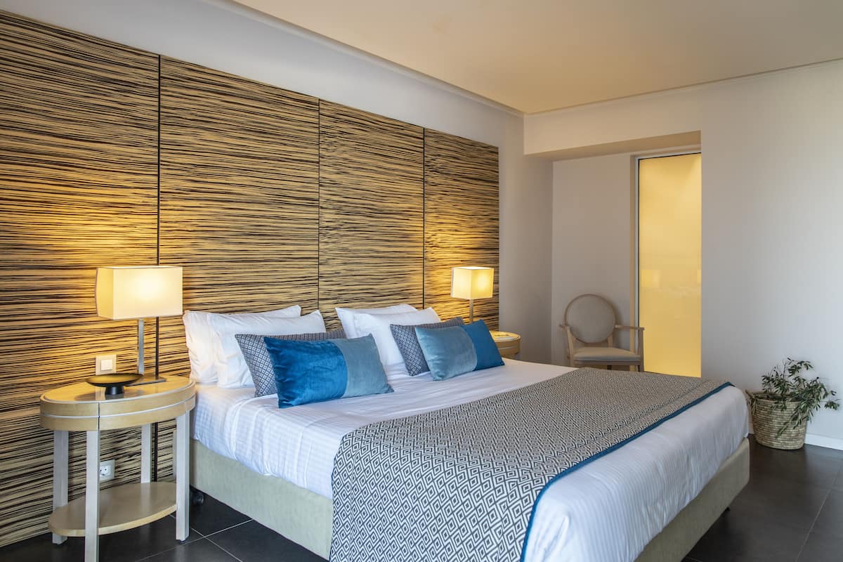 Ein modernes Schlafzimmer mit einem großen Bett, zwei Nachttischen, einem Beistelltisch und einer Topfpflanze.