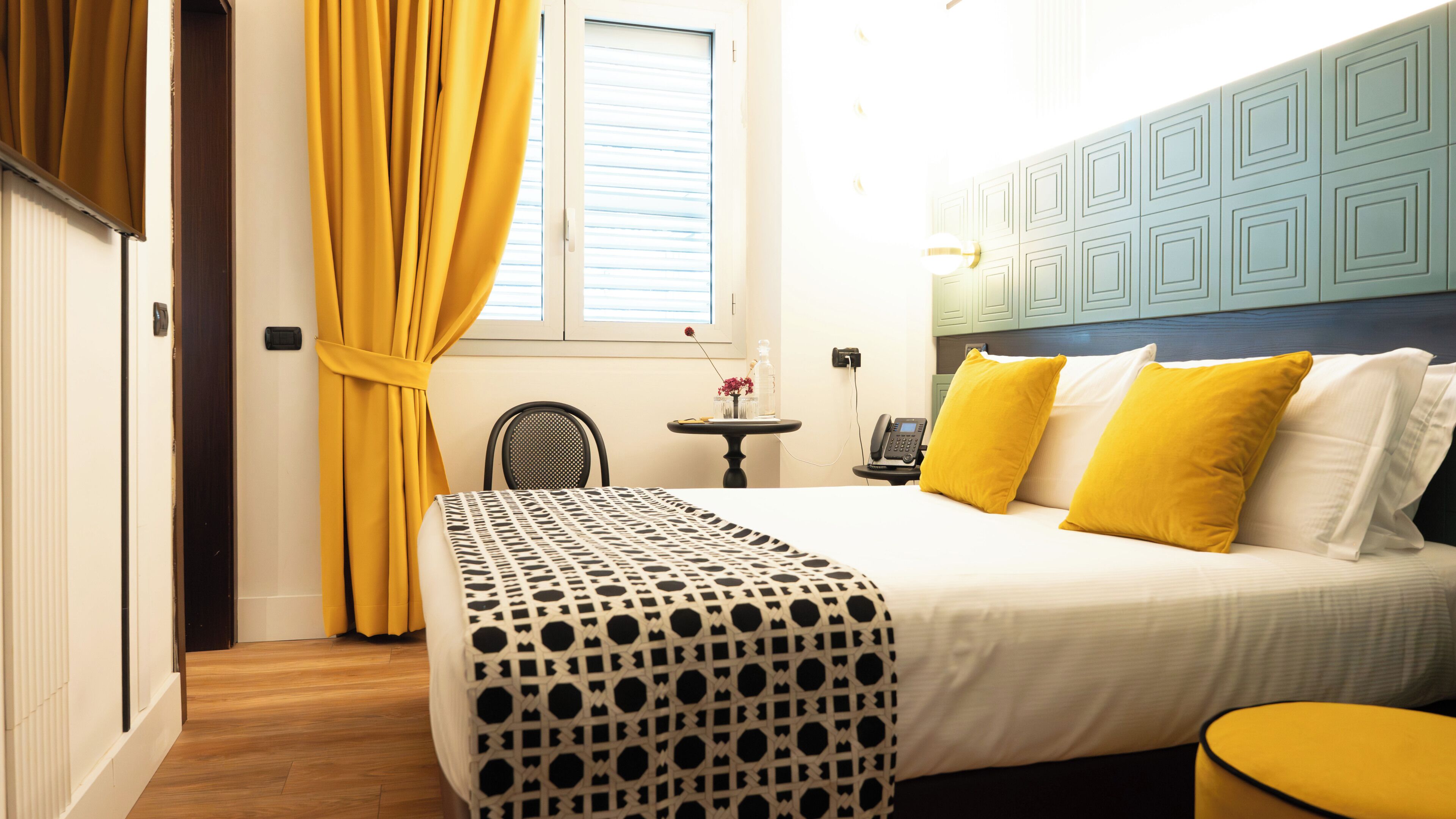 Une chambre d’hôtel avec un lit, une petite table, une chaise et une fenêtre avec des rideaux.