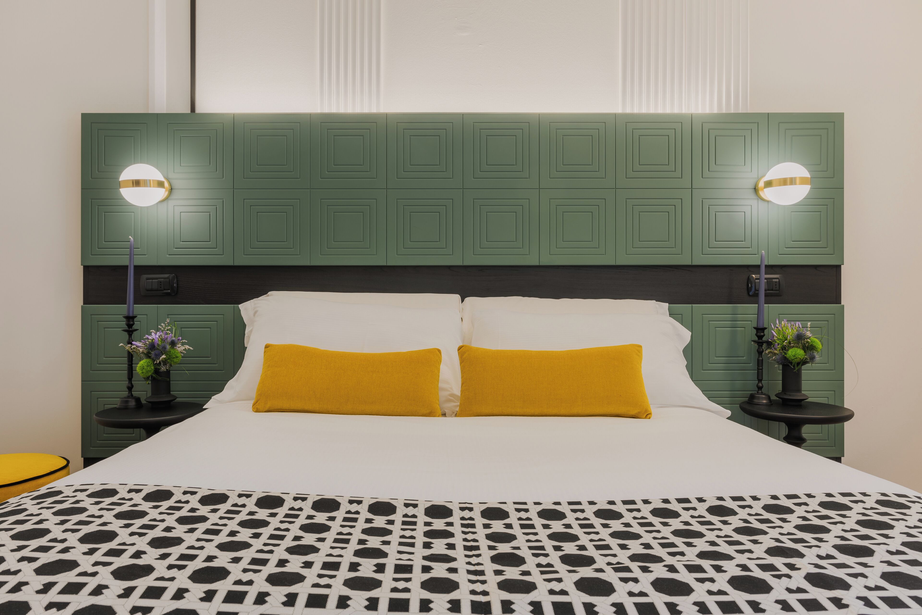 A bed with a green headboard, two bedside tables with lamps, and a patterned bedspread.