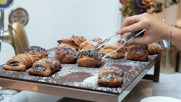 Un vassoio di pasticcini spolverati di zucchero a velo, una mano che tiene delle pinze, e uno sfondo sfocato con un cartello.