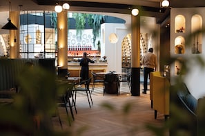 A bar area with a bartender, a seating area with tables and chairs, and a display of wine bottles. - JOIVY Together Urban Resort (Bagno a Ripoli)