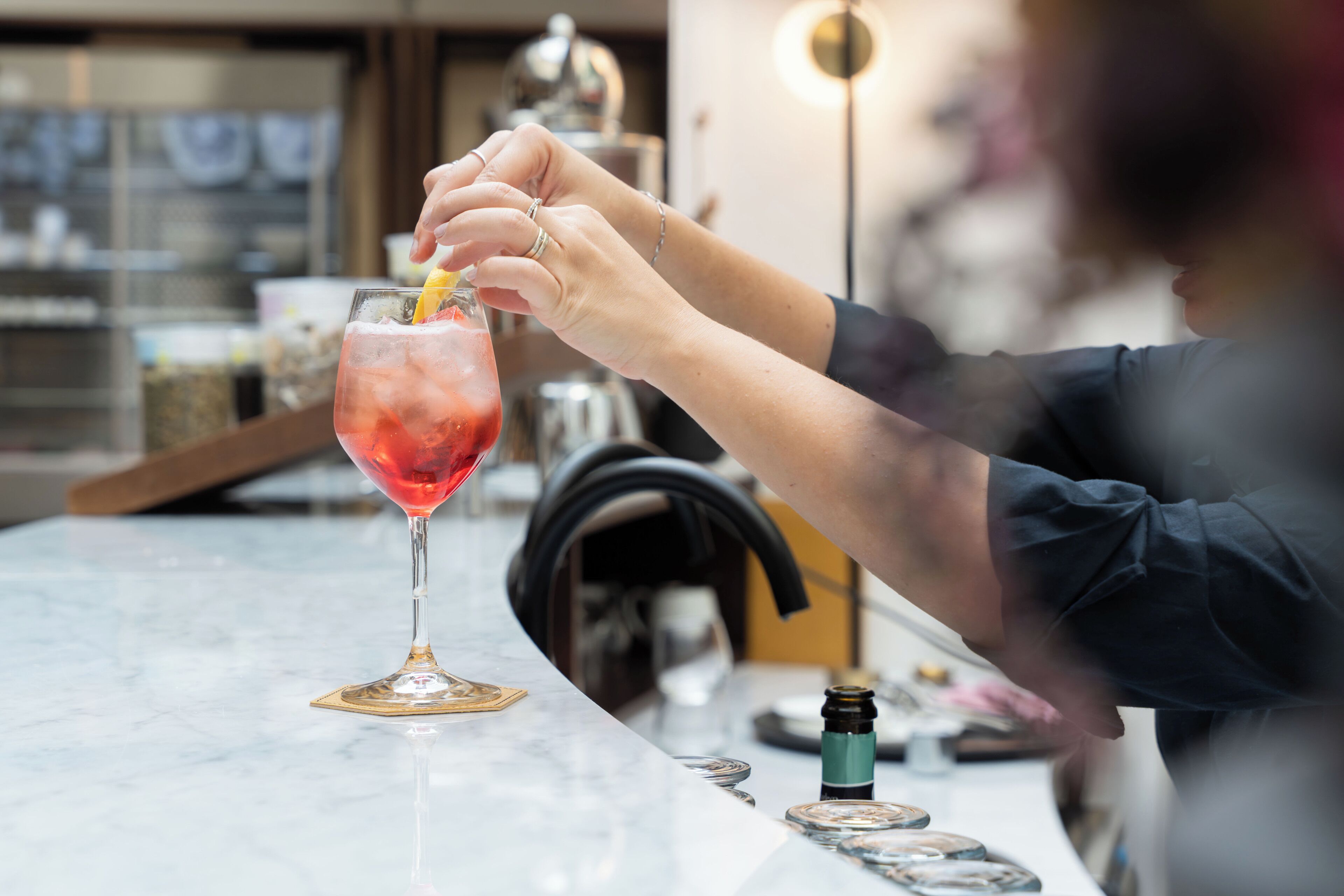 A person preparing a drink at a bar with a marble countertop and various bar tools.