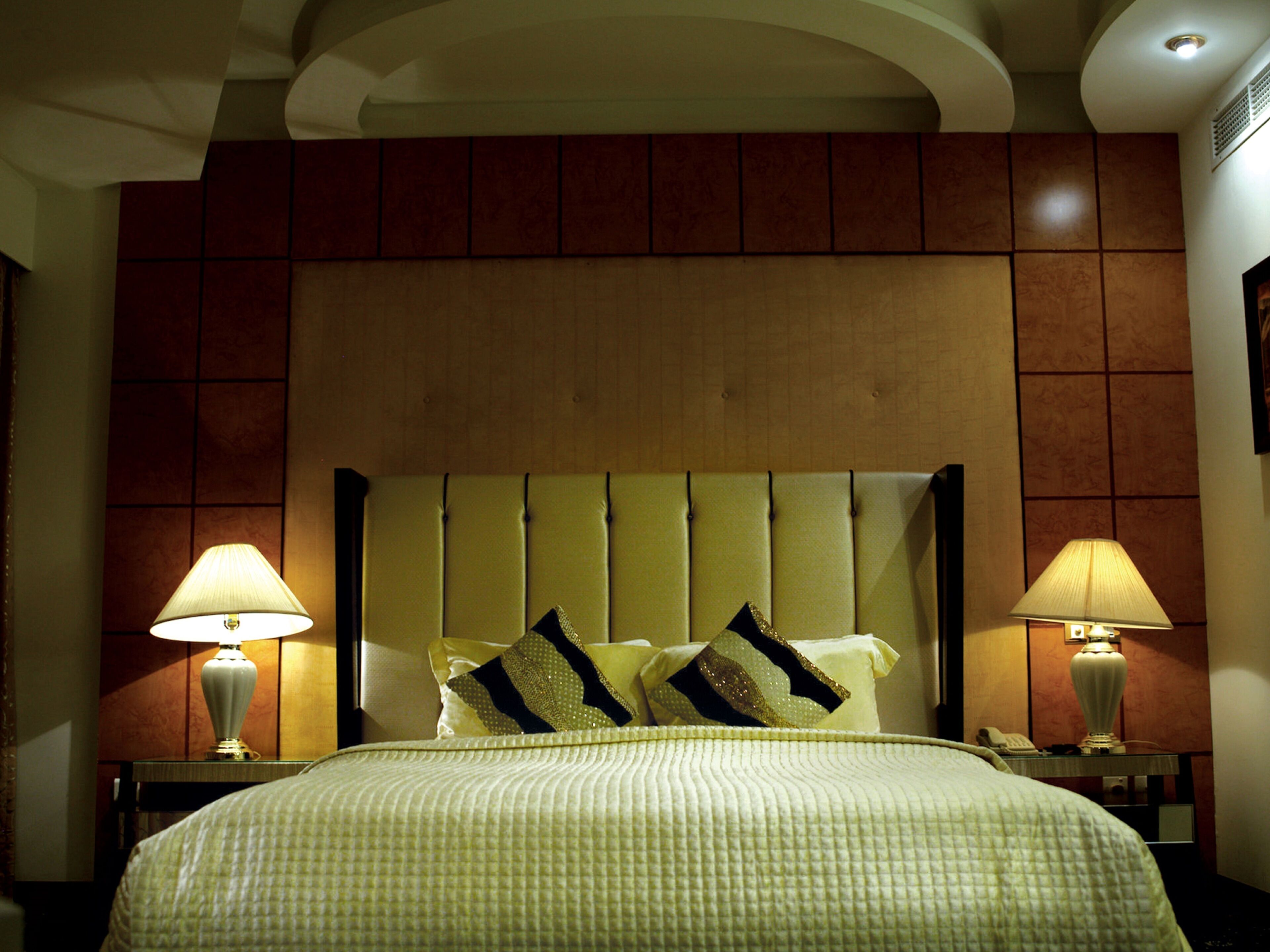Ein Hotelzimmer mit einem großen Bett, zwei Nachttischlampen, einer Kopfteil und einer Wand mit Holzvertäfelung.