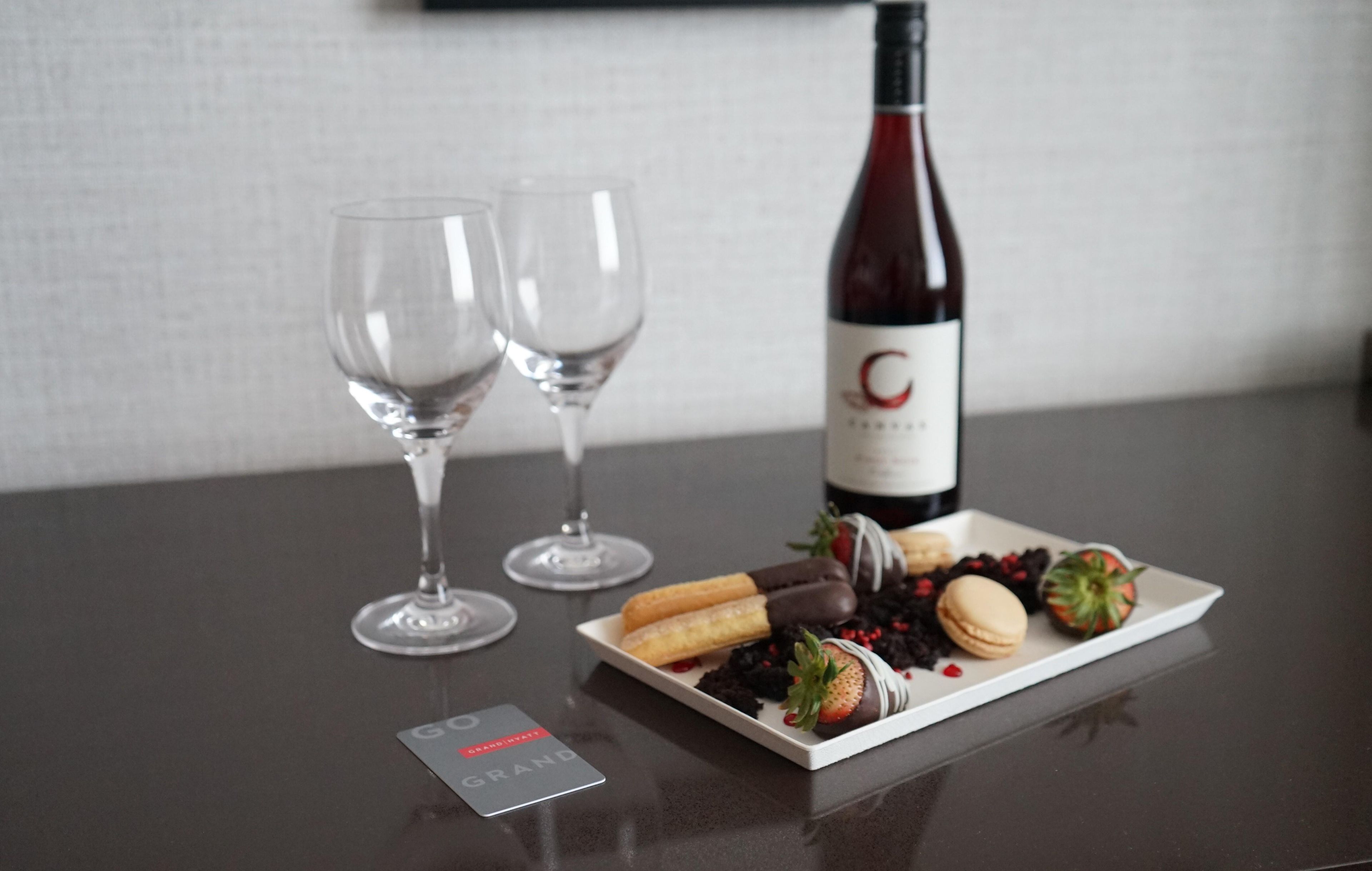 Una botella de vino, dos copas y un plato con diversos aperitivos sobre una mesa.