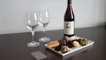 Una botella de vino, dos copas y un plato con diversos aperitivos sobre una mesa.