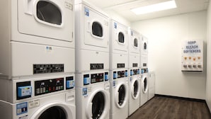 A laundry facility with multiple rows of front-loading washing machines, a soap and bleach softener dispenser, and a digital display for each machine. - Grand Hyatt San Antonio River Walk (San Antonio)