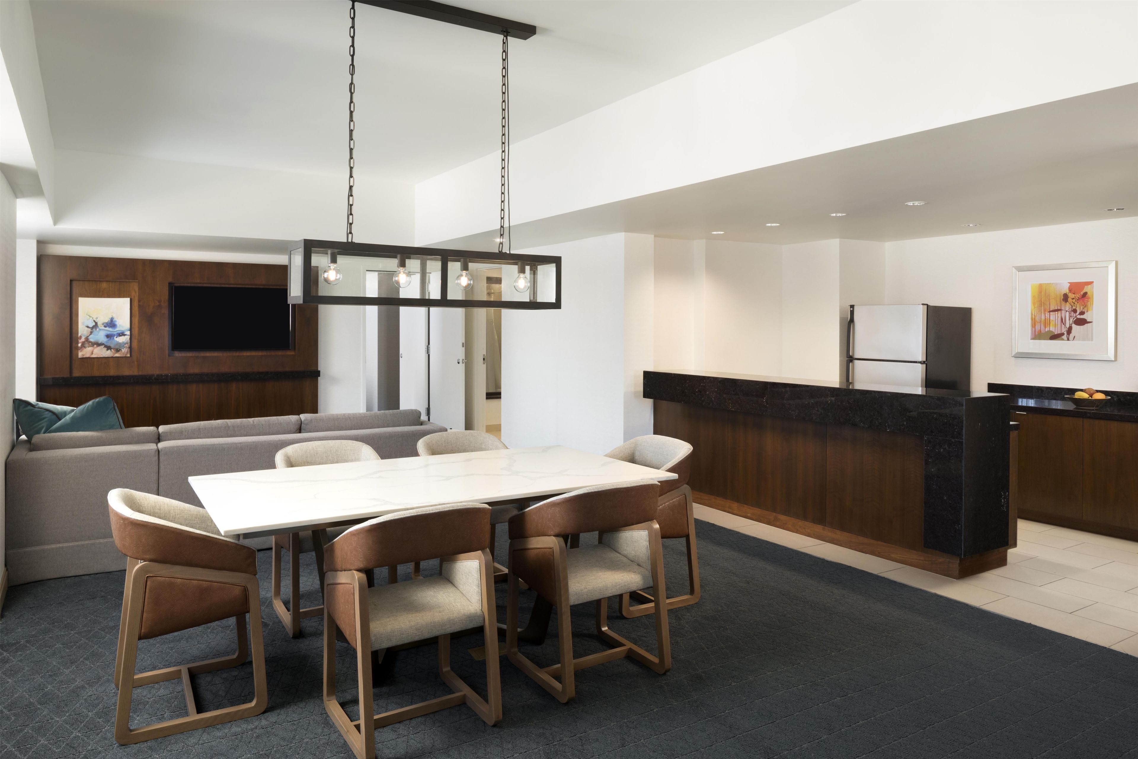 A modern kitchen with a black countertop, a built-in refrigerator, and a flat-screen TV mounted on the wall.