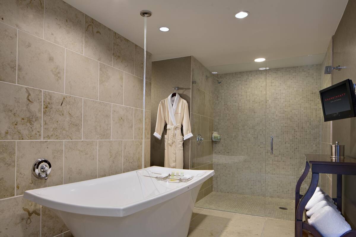 A modern bathroom with a freestanding bathtub, a glass-enclosed shower, and a flat-screen TV mounted on the wall.