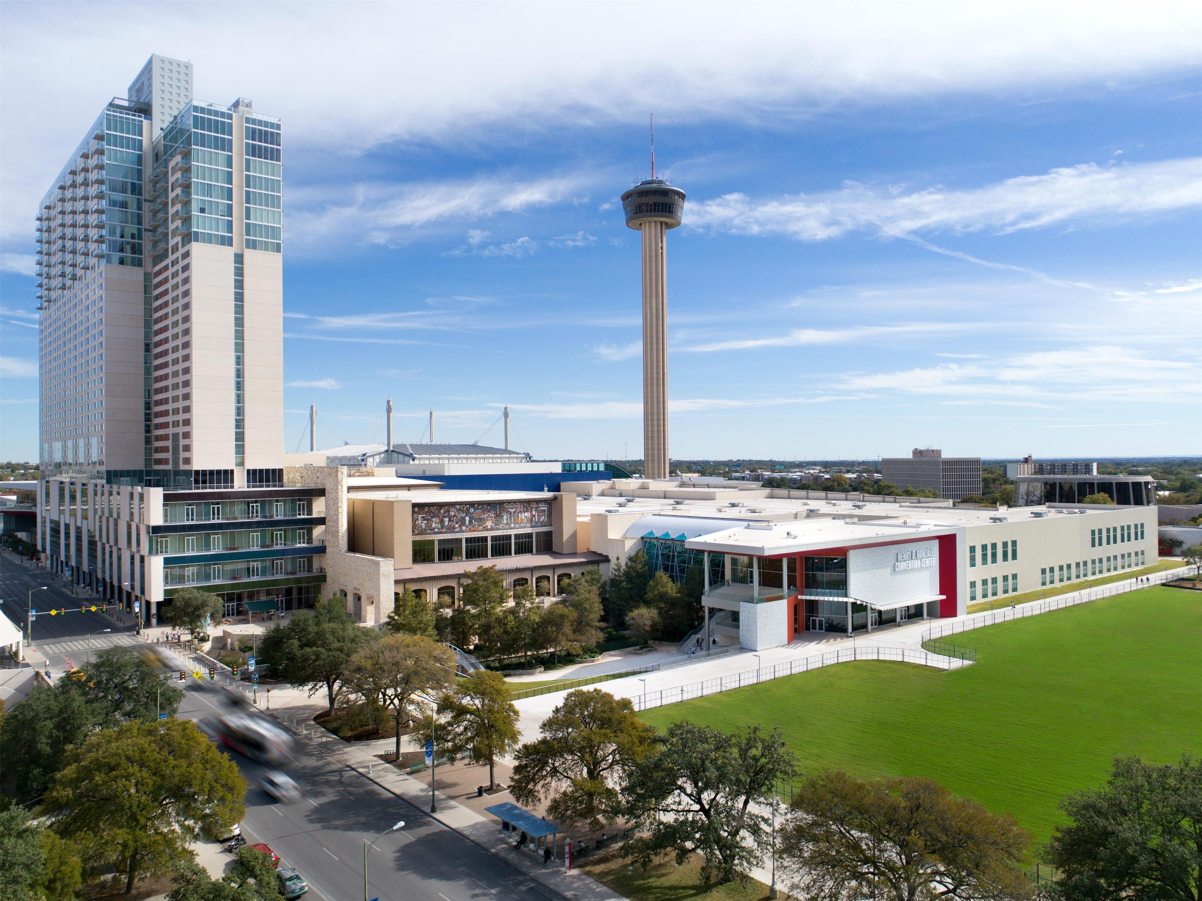 A modern building with a tower, a large green field, and a busy street.