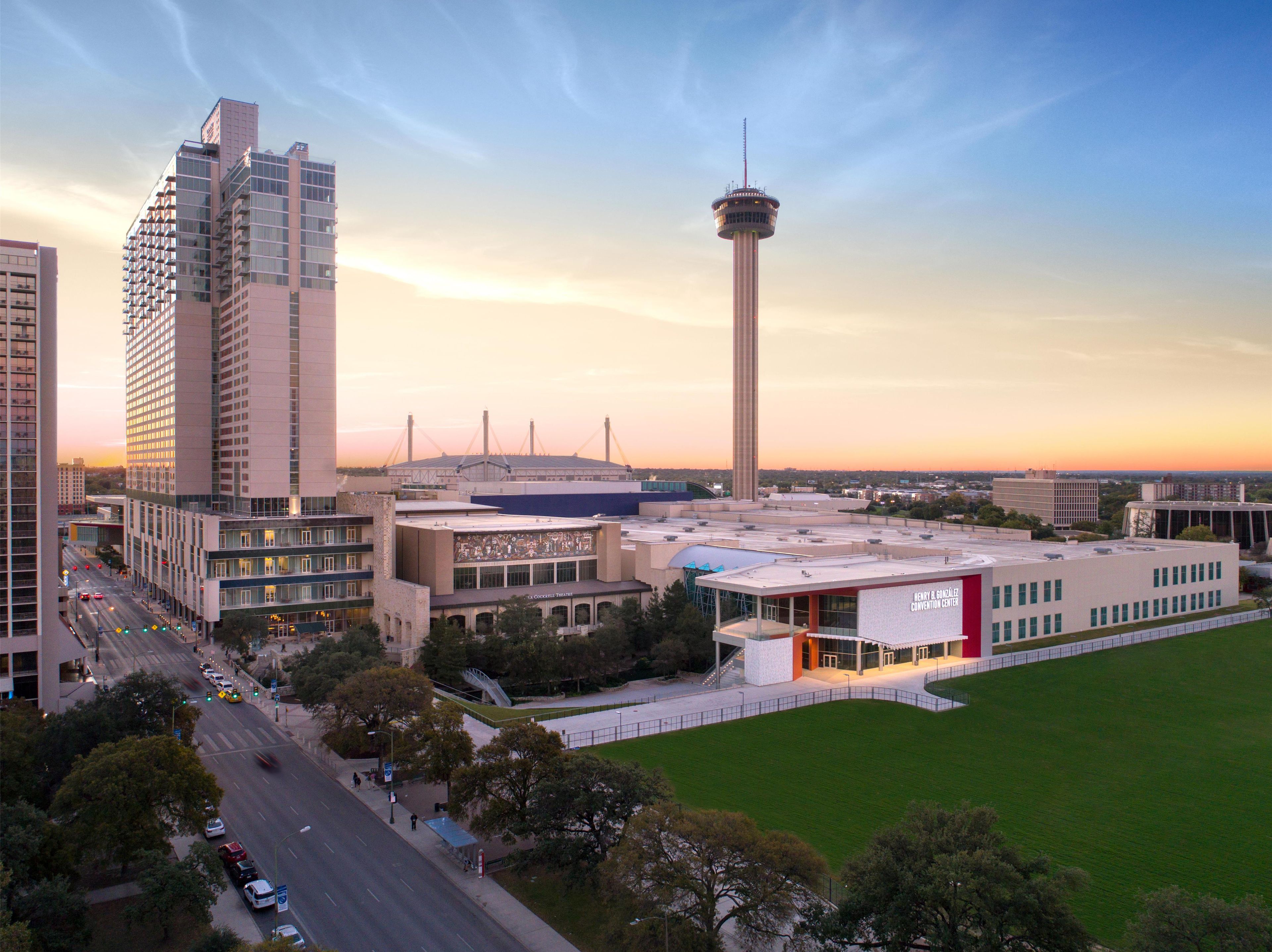 A cityscape with a prominent tower, modern buildings, and a large open green space.