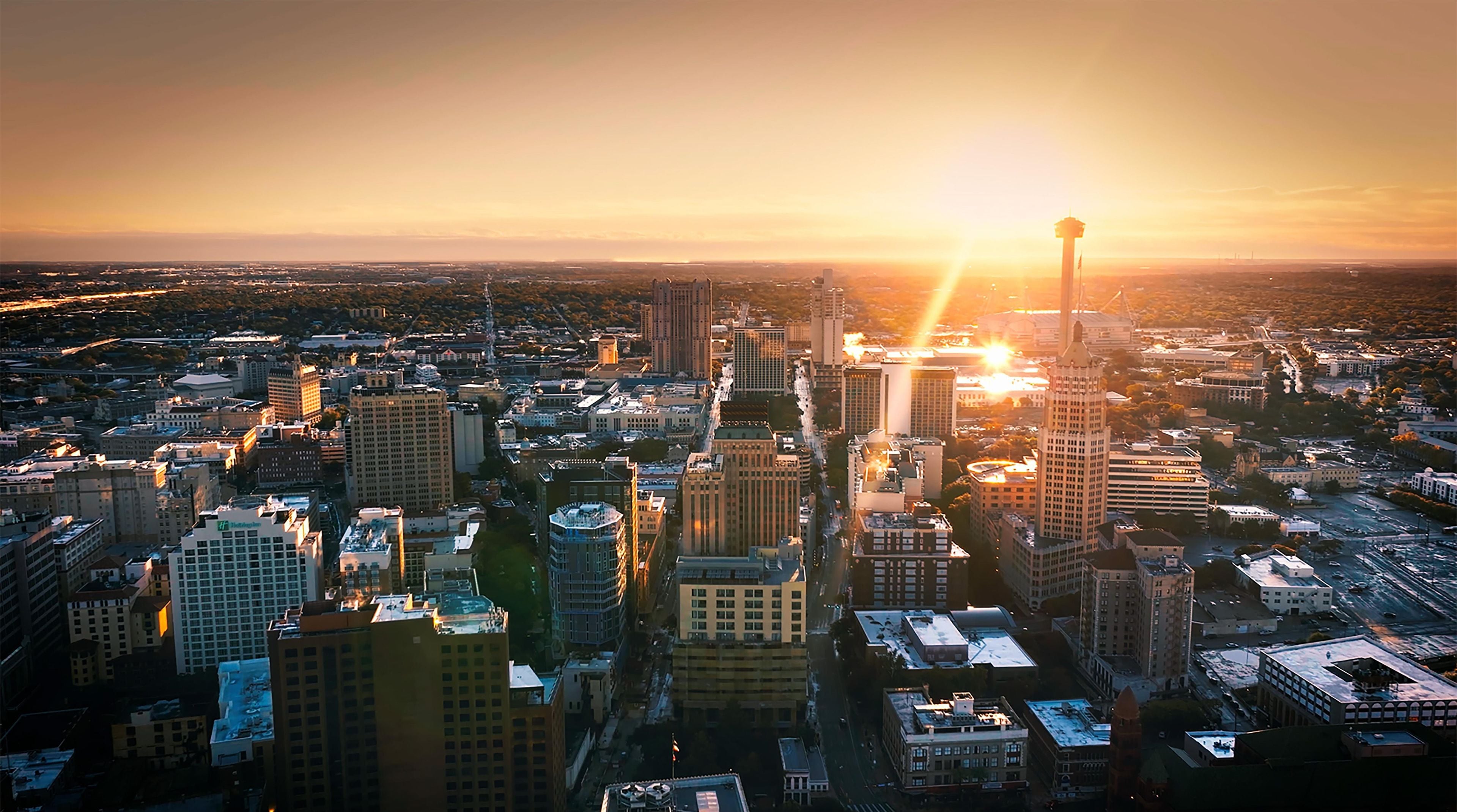 A cityscape with high-rise buildings, a prominent tower, and a sunset.