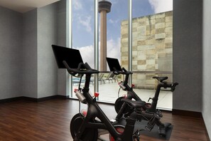 A room with two stationary bikes, a large window with a view of a tower, and a wooden floor. - Grand Hyatt San Antonio River Walk (San Antonio)