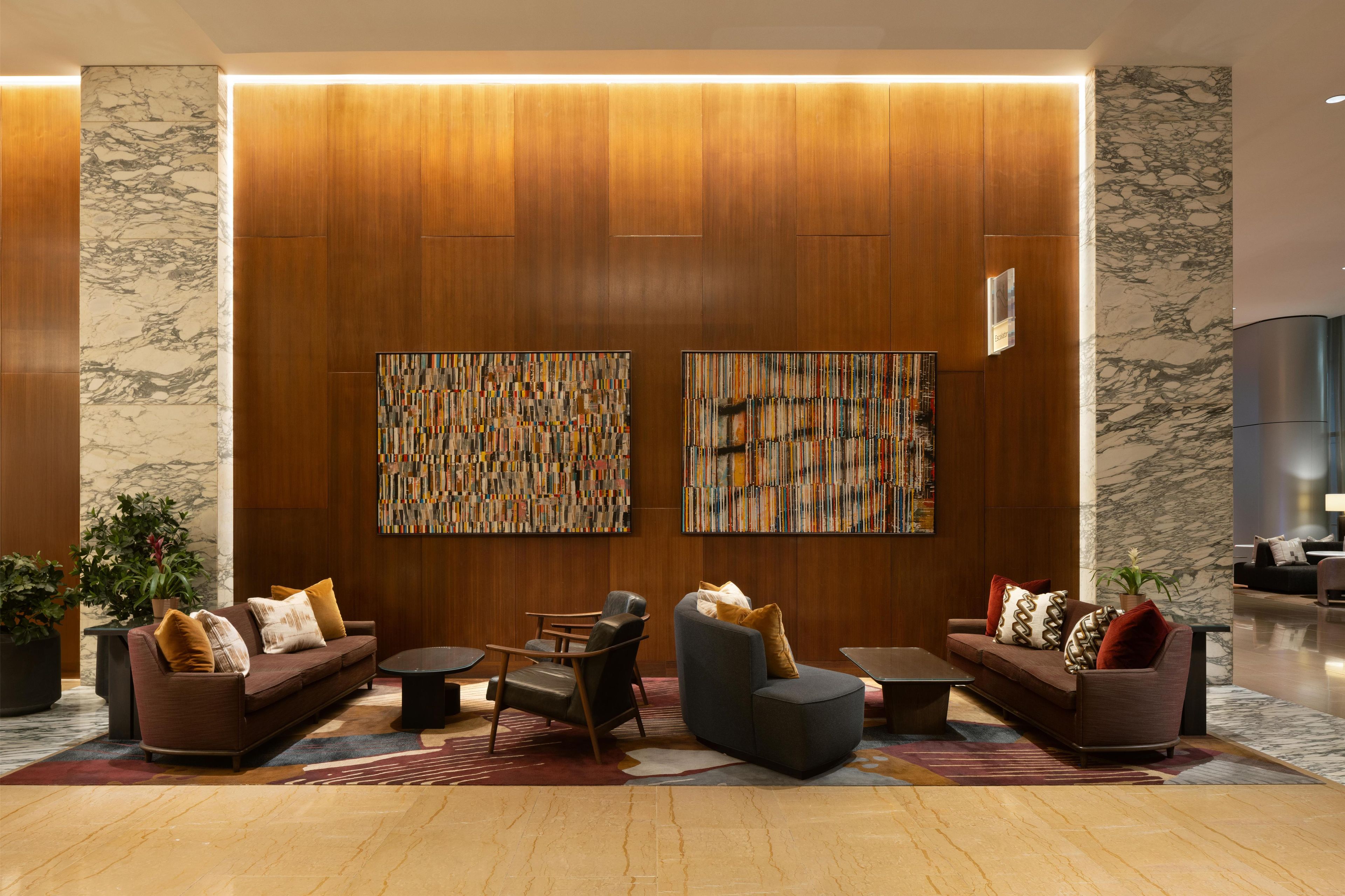 A lobby with a wooden wall, two abstract paintings, a sofa, a chair, and a coffee table.