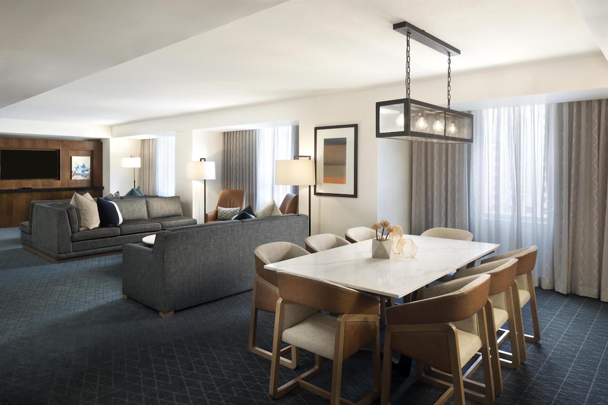 A modern hotel room with a dining area, sofa, and a flat-screen TV.