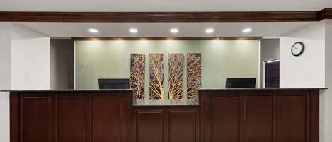 A reception desk with a wooden finish, a clock on the wall, and a decorative wall panel.