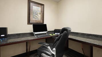 A hotel office with a desk, laptop, chair, and framed artwork on the wall.
