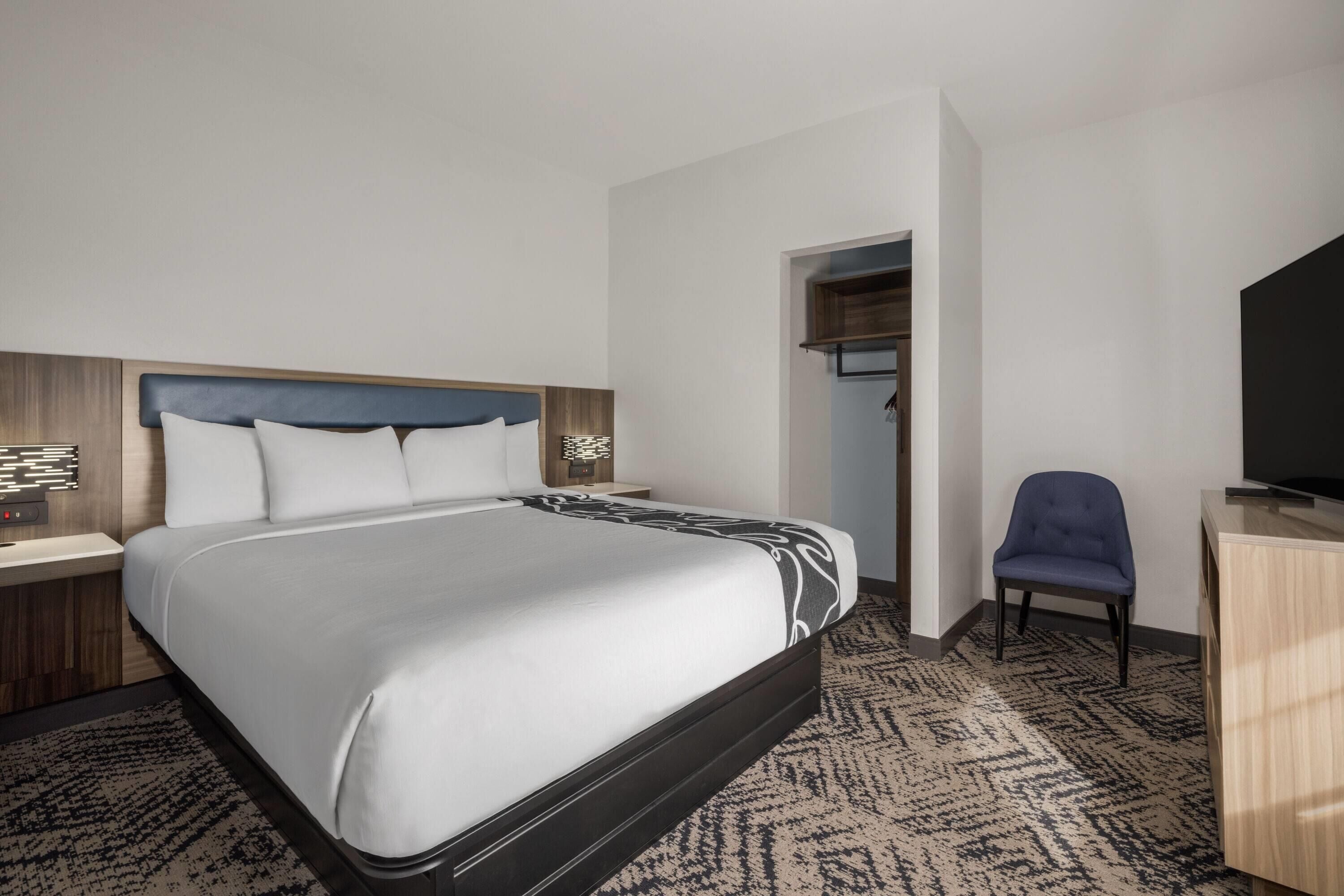 Una habitación de hotel con cama, escritorio, silla, televisor y armario.