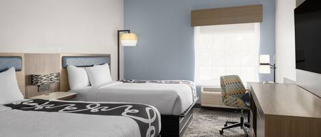 A hotel room with two beds, a desk, a chair, a TV, and a window.
