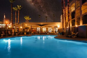 A swimming pool with lounge chairs and palm trees, surrounded by a building with balconies and string lights. - MOXY Phoenix Tempe/ASU Area (Tempe)