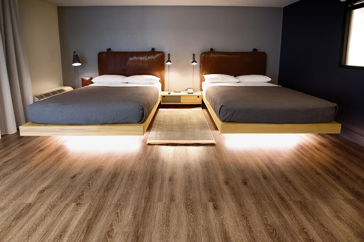 A double bed room with a wooden floor, two bedside tables, and a window.