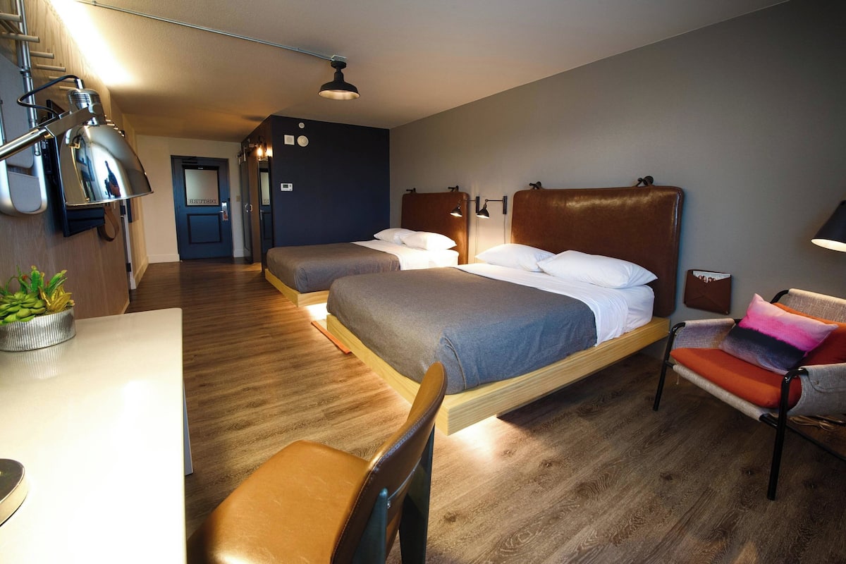 A hotel room with two beds, a desk, a chair, and a small table.