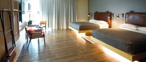 A modern hotel room with a wooden floor, two beds, a desk, a chair, and a TV.