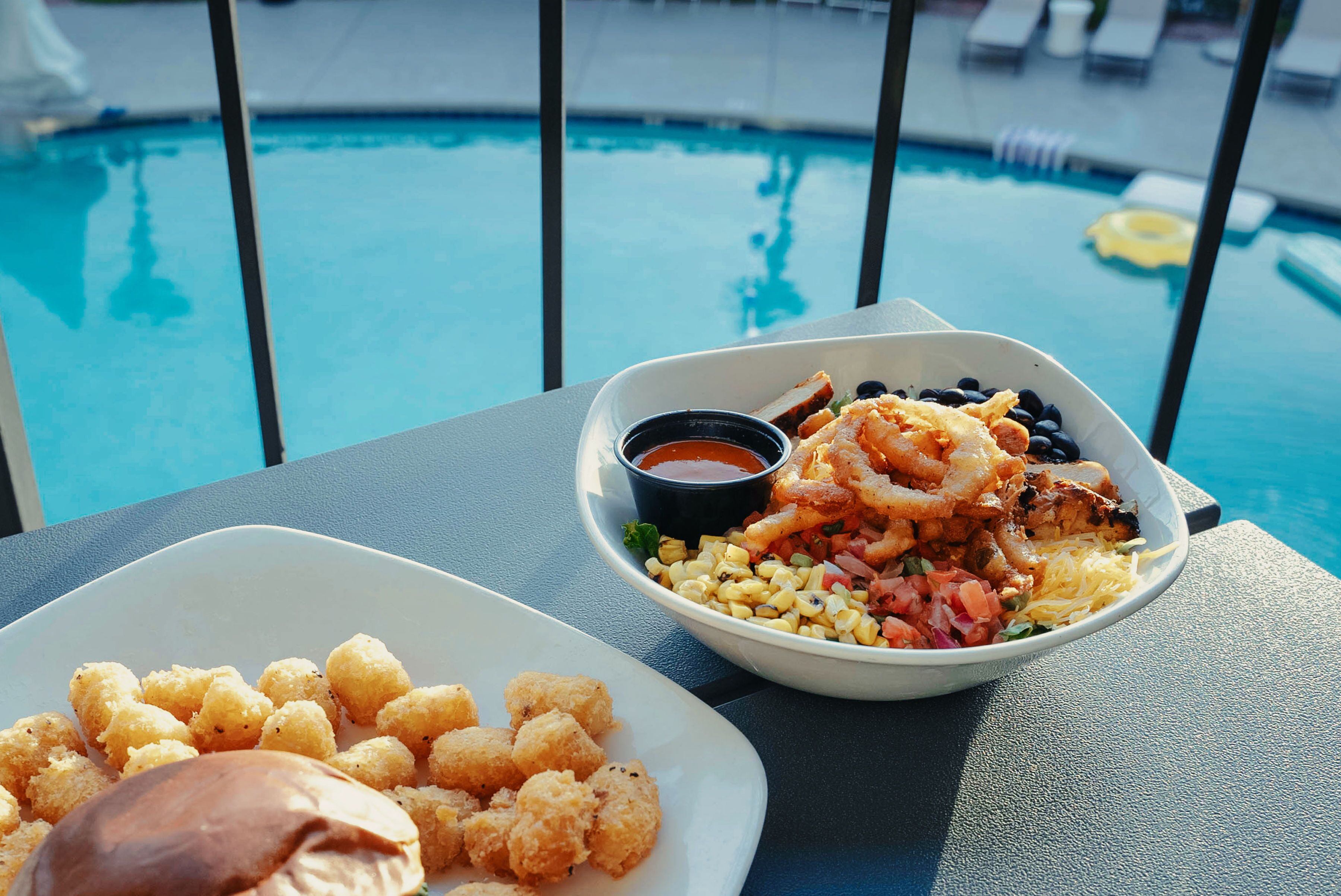A dining table with a seafood dish and a dessert, overlooking a swimming pool.