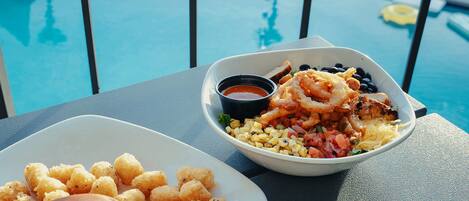 A dining table with a seafood dish and a dessert, overlooking a swimming pool.