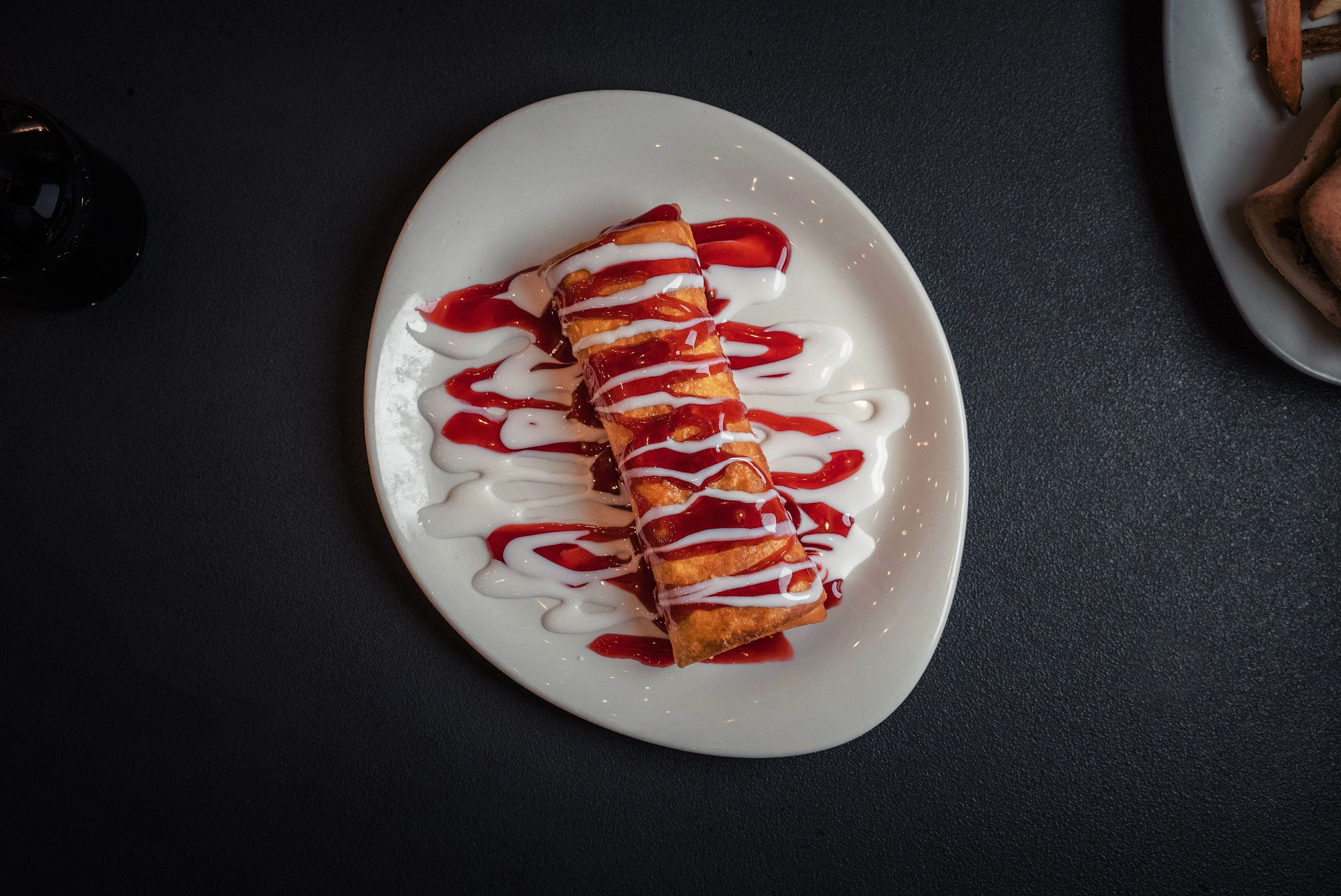 A white plate with a food item drizzled with white and red sauces.