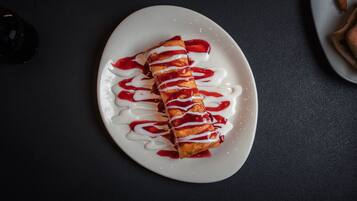 A white plate with a food item drizzled with white and red sauces.