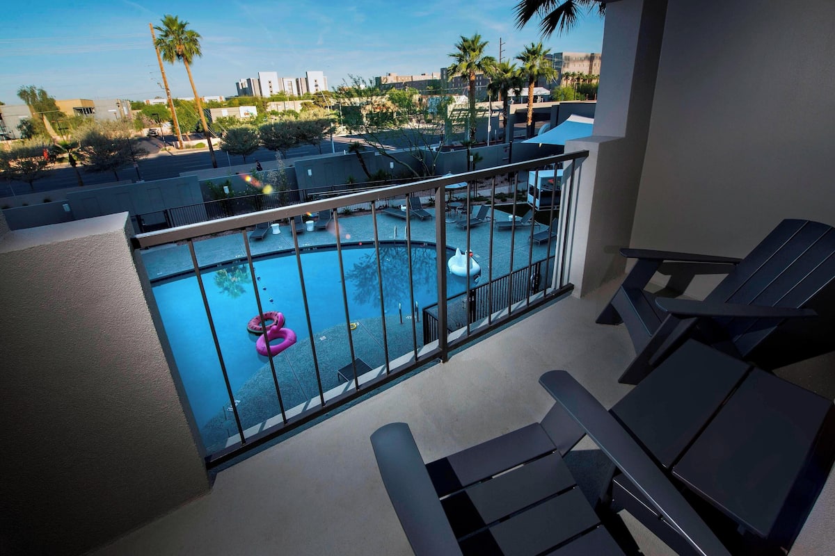 A rooftop pool area with lounge chairs, a pool, and palm trees in the background.