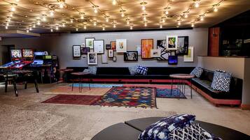 Un espace de détente moderne avec un canapé, des fauteuils et une petite table. Plusieurs écrans et œuvres d’art ornent le mur.