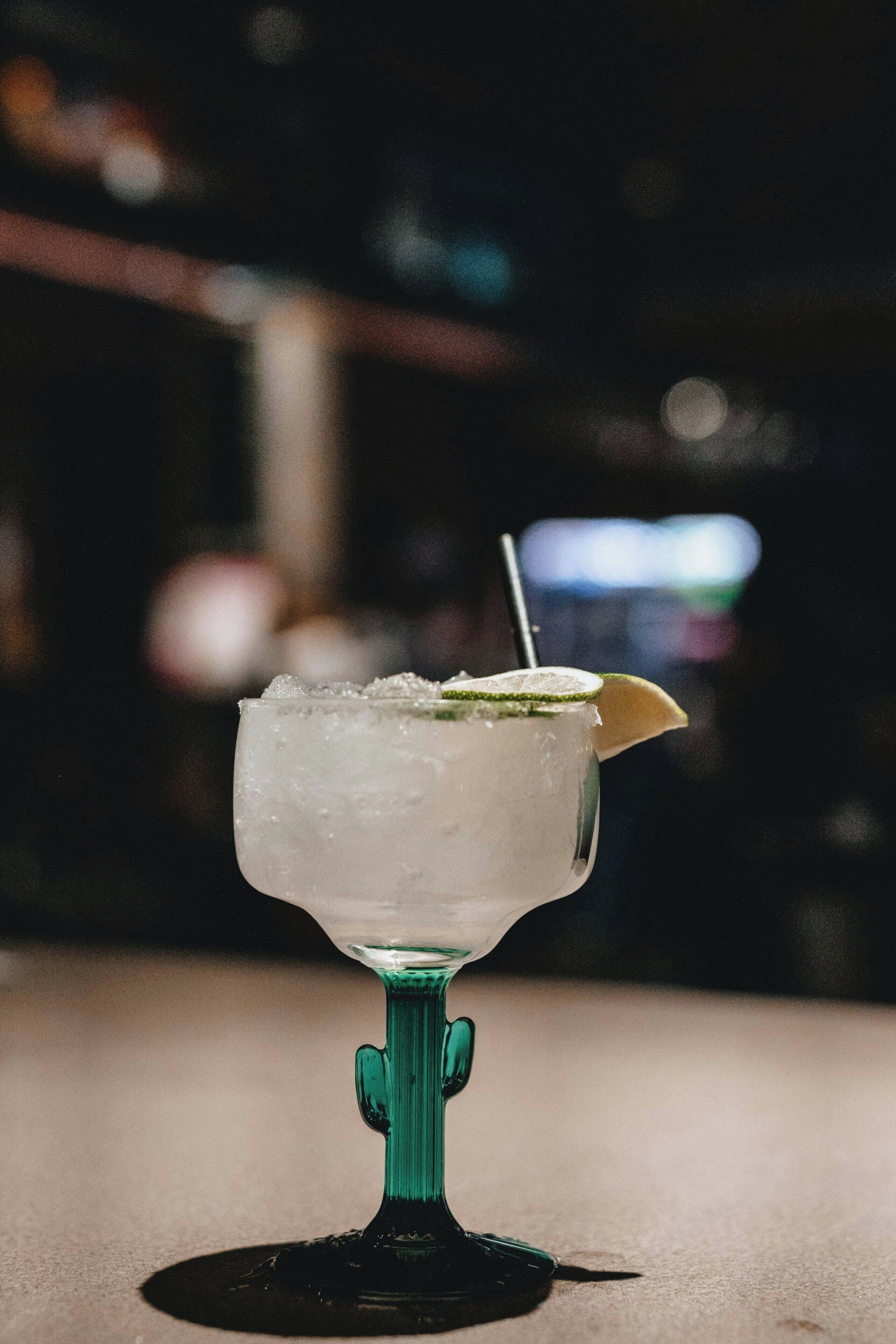 A cocktail in a green glass with ice and a lime garnish on a bar counter.