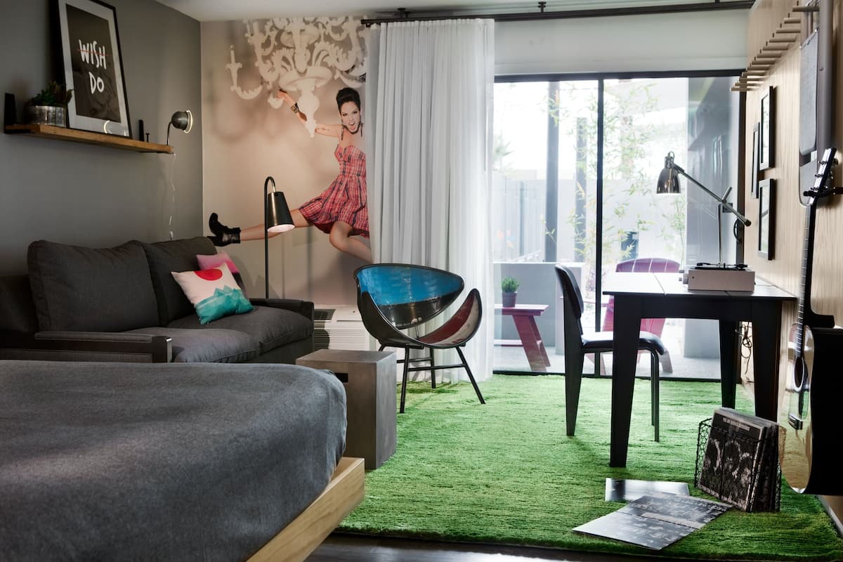 A modern bedroom with a grey sofa, a blue chair, a green rug, and a desk with a lamp.