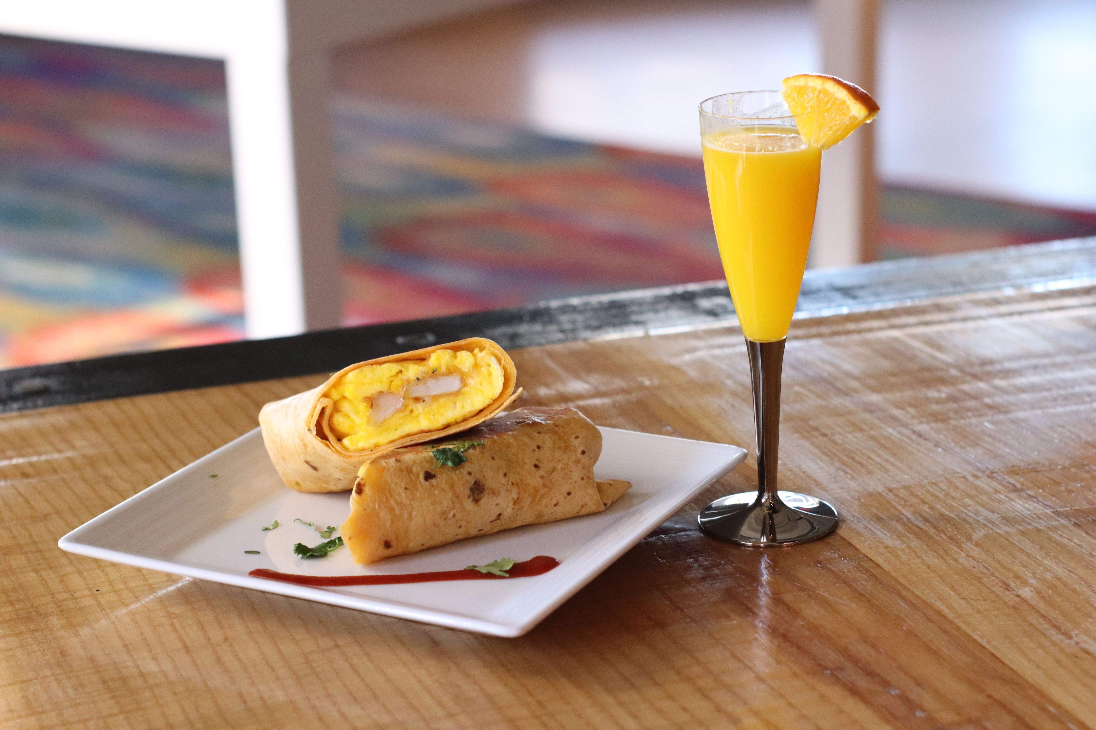 Un plato con un wrap y un vaso de jugo de naranja sobre una mesa de madera.