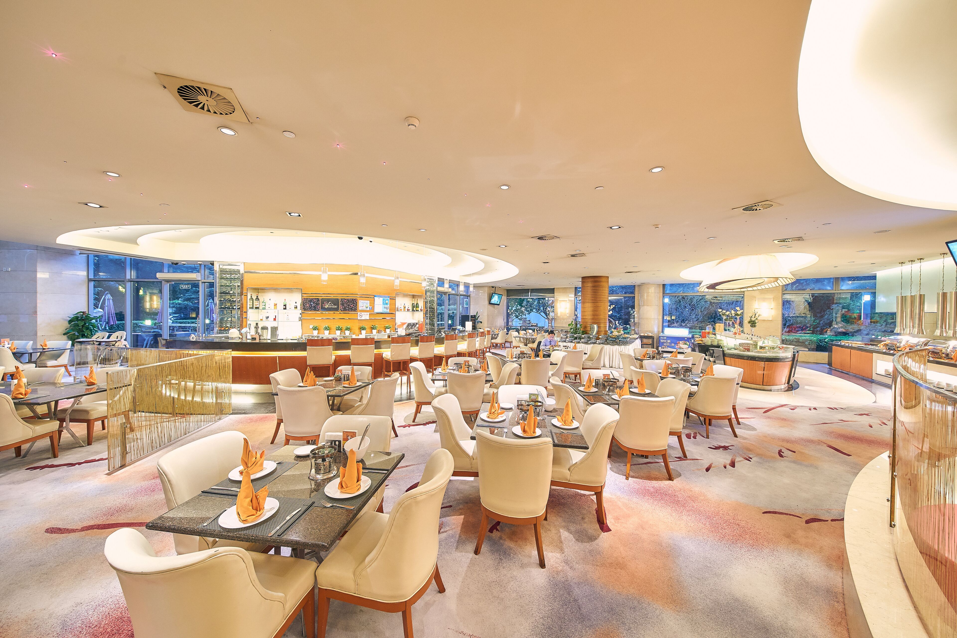 A spacious restaurant with multiple dining areas, a bar, and a view of the cityscape.