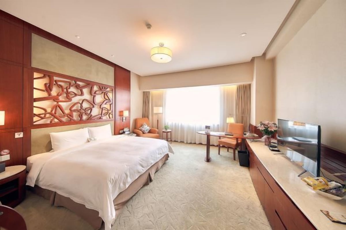 Habitación de hotel con una cama grande, un escritorio, un televisor y vistas al exterior.