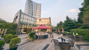 A rooftop terrace with outdoor seating, a red umbrella, and a modern building in the background. - Parkview Hotel Shanghai (Shanghai)