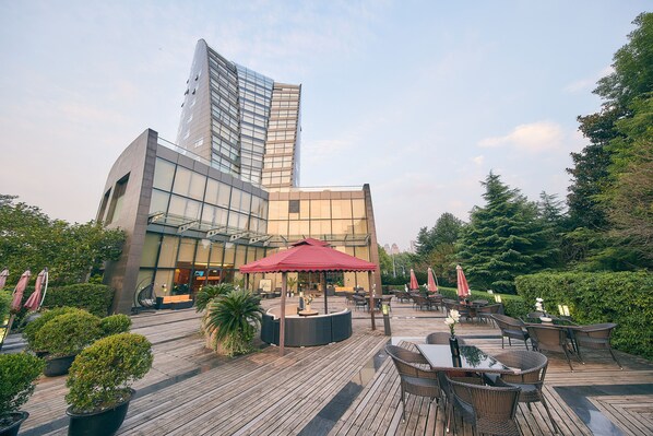 A rooftop terrace with outdoor seating, a red umbrella, and a modern building in the background.