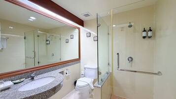 A bathroom with a granite sink, a toilet, a glass shower enclosure, and a large mirror.